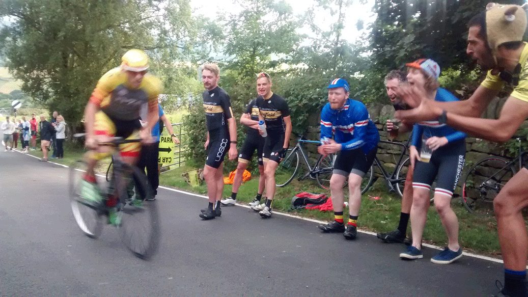 Road bike cyclist races up hill during cycle race as spectators cheer